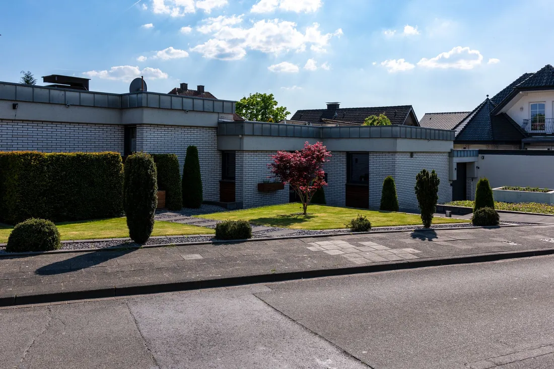 Flachdachbungalow aus hellem Klinker mit Hecke und rotem Ahorn an der Wohnstraße