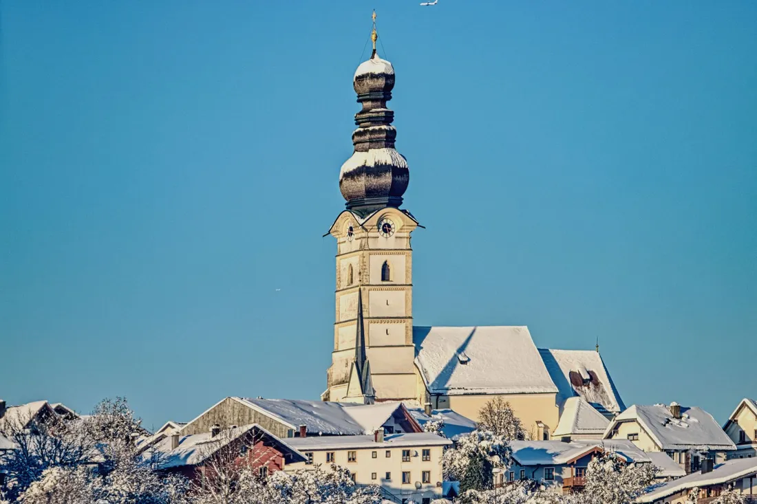 Zwiebelturm einer Dorfkirche ragt über verschneite Hausdächer in den blauen Himmel