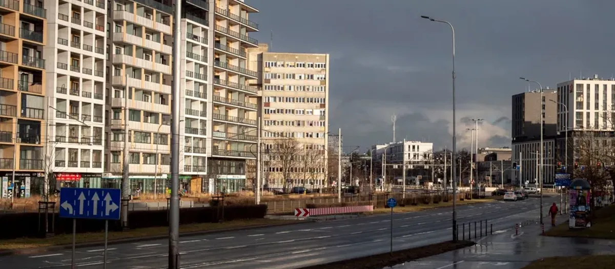 Mehrspurige Einfallstraße mit blauem Fahrstreifenschild vor hohen Wohnblocks